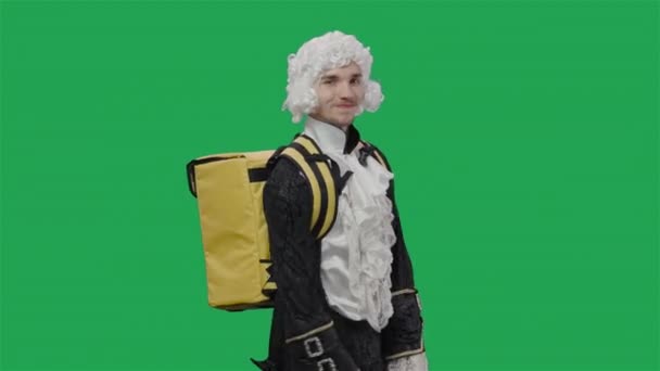 Portret dżentelmena w czarnym klasycznym garniturze i peruce, spacerującego z dużą żółtą lodówką plecaka. Młody człowiek pozujący w studio z zielonym ekranem w tle. Zamknij drzwi. Gotowy do zwolnień 59.94fps. — Wideo stockowe