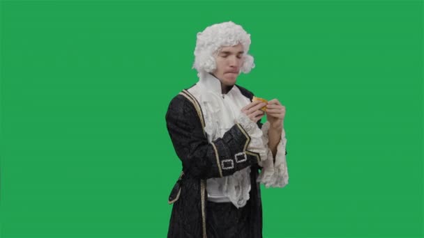 Portrait de courtisan en costume vintage historique noir et perruque, mangeant gourmand cheeseburger. Jeune homme posant en studio avec fond d'écran vert. Ferme là. Ralenti prêt 59.94fps. — Video