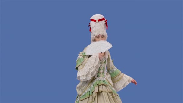 Retrato de dama cortesana en vestido de encaje vintage blanco y peluca está agitando un ventilador. Mujer joven posando en el estudio con fondo de pantalla azul. Movimiento lento. — Vídeos de Stock