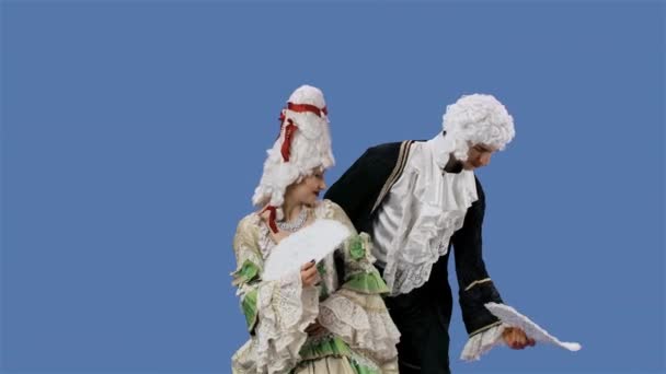 Retrato de cortesana dama y caballero en trajes históricos vintage y peluca está agitando un ventilador. Mujer joven y hombre posando en el estudio con fondo de pantalla azul. Movimiento lento. — Vídeo de stock