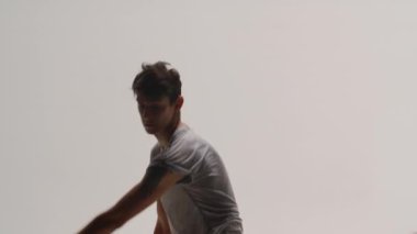 Beyaz stüdyo arka planında modern bale yapan adamın duygusal performansı. Dansçı zarif hareket eder, döner, zıplar ve amuda kalkar. Kapatın. Yavaş çekim.