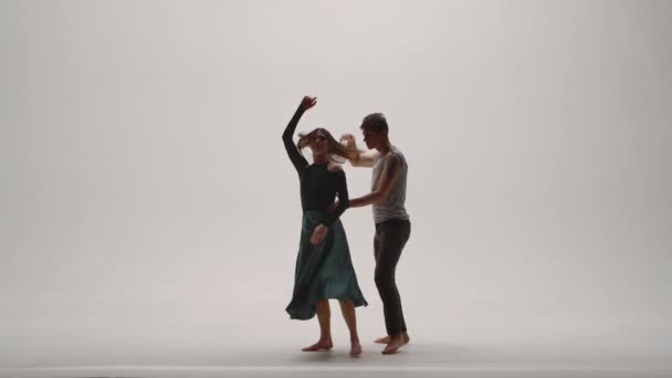Elementy nowoczesnej choreografii, współczesnej w wykonaniu młodej pary tancerzy na białym tle pracowni. Mężczyzna i kobieta tańczą namiętnie, wyrażając swoje uczucia w tańcu. Zwolniony ruch. — Wideo stockowe