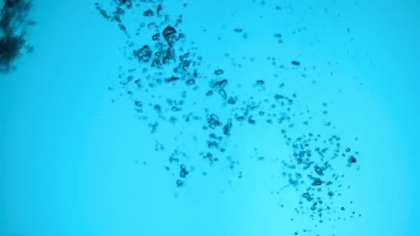 Поток воды в замедленной съемке падает в резервуар с водой, создавая пузырьки воздуха, капли брызг после падения. свежесть прозрачной голубой жидкости, вылитой в прозрачный контейнер на синем фоне — стоковое видео