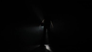 Karanlıktan ve dumandan, elinde bir basket topuyla kameraya doğru yürüyen bir adam silueti. Basketbolcu arka farıyla stüdyoda poz veriyor. Yavaş çekim hazır 59.94fps.