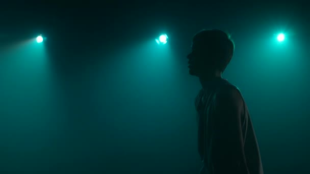 La silueta de un jugador de baloncesto joven practicando arroja sobre un fondo de estudio oscuro con humo y luces azules. De cerca. Vista lateral. Cámara lenta lista 59.94fps. — Vídeo de stock