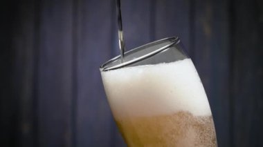Hafif bira siyah arka plandaki bir bardağa dökülür. Dolu bir bardaktan kalın beyaz köpük akar. El yapımı bira konsepti. Ağır çekim. Kapat..