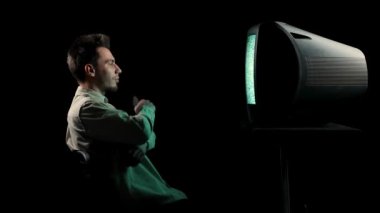 Eski bir televizyonun önünde siyah bir arka planda oturan bir adamın yan görüntüsü. Adam uzaktan kumandayı alıyor, kanalları değiştiriyor, gülümsüyor, şaşırıyor, başını sallıyor, esniyor. Kapat..