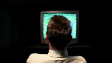 Arka planda, karanlık bir stüdyoda eski bir televizyonun önünde oturan bir adam var. Gürültü paraziti ya da televizyon ekranındaki hatlar, bozuk ve terk edilmiş retro TV. Kapat..