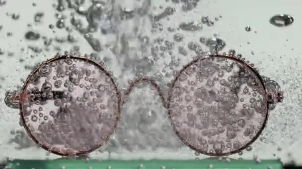 Un jet de soude est versé sur des verres ronds dans l'eau, provoquant un tourbillon de bulles d'oxygène. Verres dans l'eau sur fond blanc. Au ralenti. Gros plan. — Video