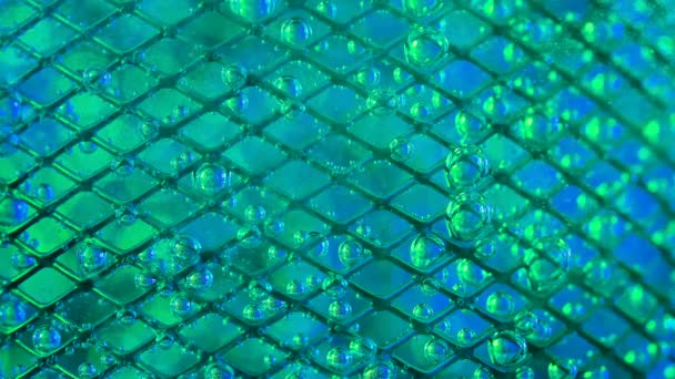 The flow of water directed to the metal mesh causes the bubbling of oxygen bubbles. Mesh in water, covered with iridescent oxygen bubbles due to a blue green blurred background. Slow motion. Close up. — стоковое видео