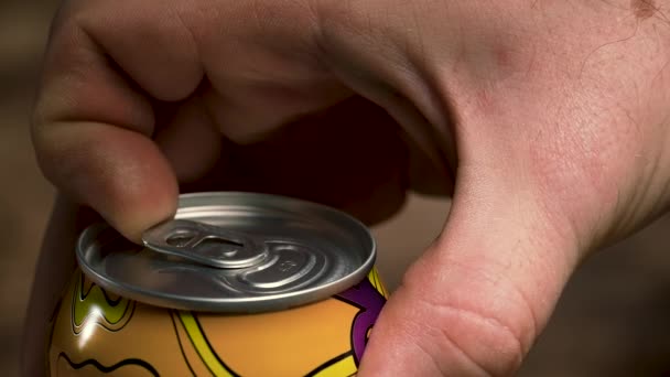 The mans hands open a shaken can of beer, a frothy cold drink pours out of it. A detailed shot of a mans hands opening a stirring beer can against a blurred background. Slow motion. — Stock Video