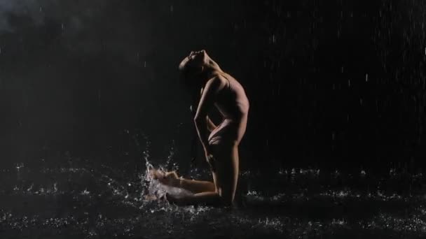 Ballerino impulsivo che balla in stile moderno con coreografia contemporanea su sfondo nero sotto la pioggia. Silhouette di giovane donna mosse vigorose e la creazione di spruzzi. Rallentatore. — Video Stock