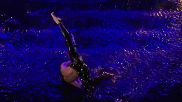 Widok z góry zmysłowy młody człowiek wykonujący nowoczesne elementy taneczne w deszczu na powierzchni wody. Mężczyzna tancerz taniec sztuki współczesnej na czarnym tle studio z niebieskim podświetleniem. Zwolniony ruch. — Wideo stockowe