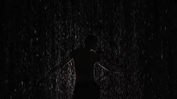 Modernes Ballett, Contest, zeitgenössischer Auftritt eines Mannes mit nacktem Oberkörper im Regen vor hellem Scheinwerferlicht. Silhouette einer Tänzerin, die sich in Zeitlupe zwischen glänzenden Regentropfen bewegt. — Stockvideo