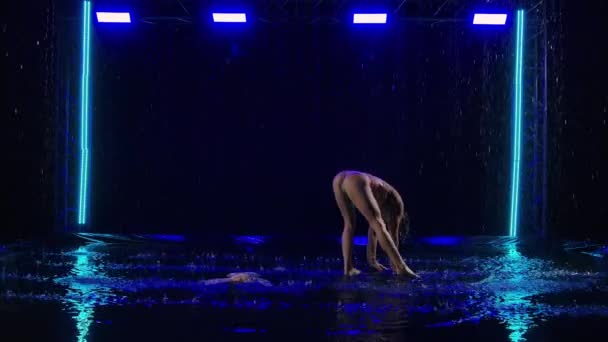 Ευγενικός στοχασμός από ευέλικτη χορεύτρια σε βροχή με φόντο σκοτεινό στούντιο με μπλε φώτα. Νεαρή βρεγμένη ημίγυμνη γυναίκα χορεύει μοντέρνα χορογραφία ανάμεσα σε σταγόνες βροχής. Αργή κίνηση. — Αρχείο Βίντεο