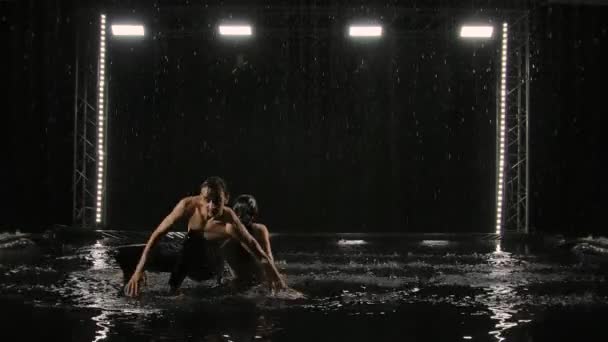 Un par de jóvenes bailarines bailan apasionadamente contemporáneos bajo la lluvia. Hombre y mujer expresan sus sentimientos y emociones a través de la danza. Oscuridad, agua, spray, pasión. Movimiento lento. — Vídeos de Stock