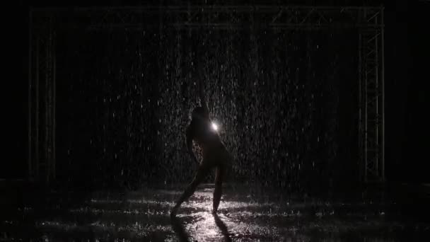 Ballet moderno, contemp, contemporáneo interpretado por mujer bajo la lluvia sobre el telón de fondo de luz brillante. Silueta de bailarina moviéndose en cámara lenta entre brillantes gotas de lluvia. — Vídeo de stock