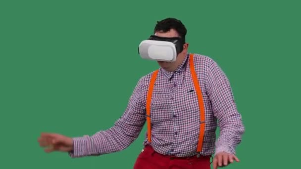 Retrato de un hombre bailando con un casco de realidad virtual o gafas 3D en la cabeza. Un hombre con gafas, una camisa con tirantes naranjas en el estudio en una pantalla verde. En cámara lenta. De cerca.. — Vídeo de stock