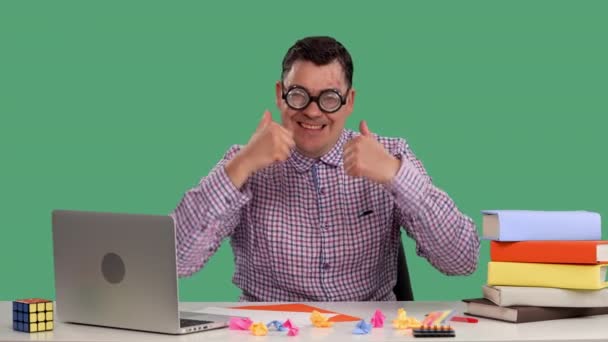 Un homme assis à un bureau devant un ordinateur portable, pense à quelque chose, puis montre un pouce vers le haut avec les deux mains. Portrait d'un homme avec des lunettes en studio sur un écran vert. Au ralenti. Gros plan. — Video