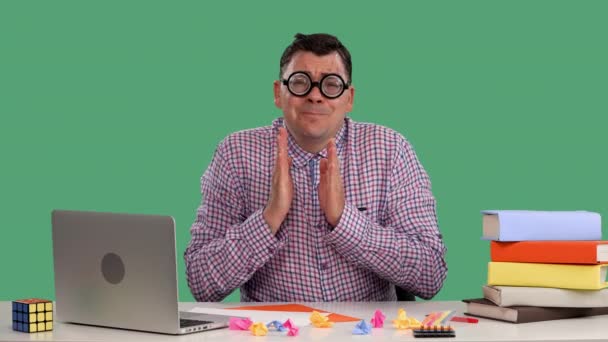 Bir adam dizüstü bilgisayarın ve kitapların önünde oturuyor ellerini bir dua jestiyle katlıyor, bir şey istiyor, bir dilek diliyor. Stüdyoda yeşil ekranda gözlüklü bir adamın portresi. Yavaş çekim — Stok video