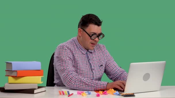 Человек сидит за столом, пользуется ноутбуком, с энтузиазмом играет в онлайн-игру, празднует победу. Портрет мужчины в студии на зеленом экране. Медленное движение. Закрыть. — стоковое видео