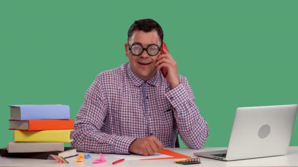Bir adam açık bir dizüstü bilgisayarın önünde masada oturuyor ve cep telefonuyla konuşuyor. Stüdyoda yeşil ekranda bir adamın portresi. Ağır çekim. Kapat.. — Stok video