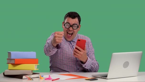 Un bărbat își verifică telefonul și sărbătorește o victorie. Portretul unui bărbat care stă la o masă în fața unui laptop din studio pe un ecran verde. Mişcare lentă. Close up . — Videoclip de stoc