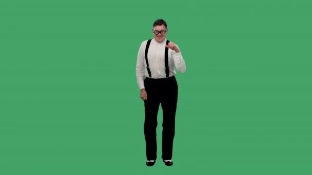 Portret van een tevreden man die danst en een duim omhoog laat zien. Een man met een bril met dikke lenzen, een wit shirt met een bretels poseert in de studio op een groen scherm. Langzame beweging. — Stockvideo