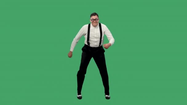 Portret van een tevreden man die brandend danst. Een man met een bril met dikke lenzen, een wit shirt met bretels danst in de studio op een groen scherm. Langzame beweging. — Stockvideo