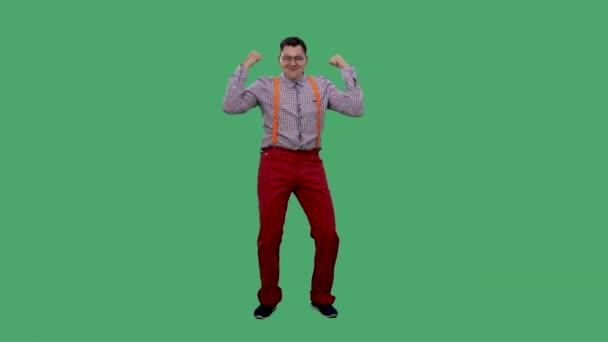Ένας ικανοποιημένος άνθρωπος χορεύει με τα χέρια ψηλά, σφίγγει γροθιές και στρέφει τα δάχτυλά του προς τον εαυτό του, γιορτάζοντας τη νίκη. Πορτρέτο ενός άντρα με γυαλιά στο στούντιο σε μια πράσινη οθόνη. Αργή κίνηση. — Αρχείο Βίντεο