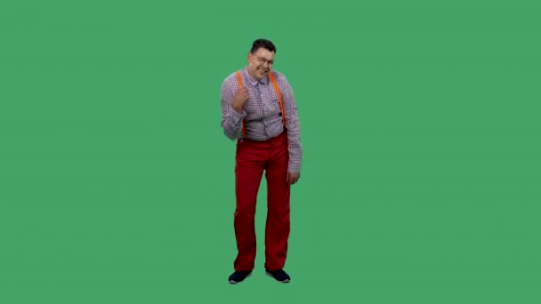 Rozmrzelý muž se líně ukáže a zeptá se, kdo jsem. Muž v brýlích v kostkované košili s oranžovými podvazky pózuje ve studiu na zelené obrazovce. Zpomalený pohyb. — Stock video