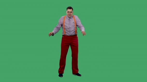 The man is dancing the dance of the robot. Portrait of a man in glasses, in a plaid shirt with orange suspenders in the studio on a green screen. Slow motion. — Stock Video