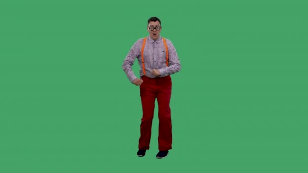 O homem dança, canta, alisa uma sobrancelha, flertando. Retrato de um homem em óculos com lentes grossas, em uma camisa xadrez com suspensórios laranja no estúdio em uma tela verde. Movimento lento. — Vídeo de Stock