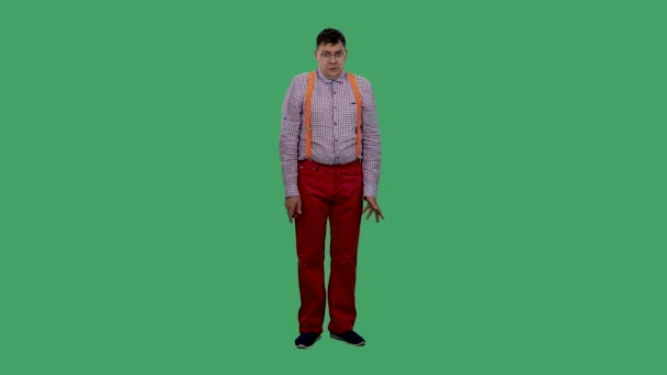 De man haalt zijn schouders op en schudt zijn hoofd. Portret van een man in een bril, in een geruit shirt met oranje bretels in de studio op een groen scherm. Langzame beweging. — Stockvideo
