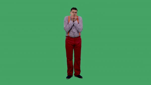 Ein Porträt eines Mannes, der geradeaus blickt und seine Hände vor Angst zu einer Faust an sein Kinn presst. Ein Mann mit Brille, in einem Hemd mit orangefarbenen Hosenträgern im Studio auf einer grünen Leinwand. Zeitlupe. — Stockvideo