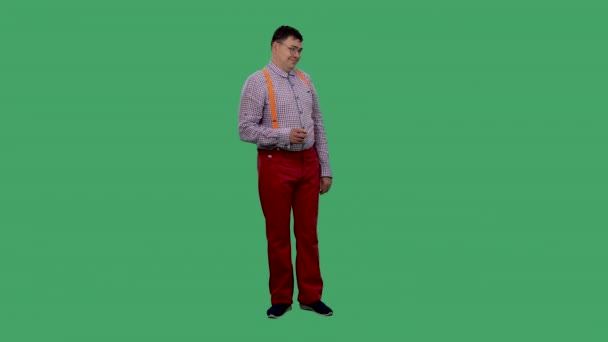 The man raises his eyebrows, flirting, and points his index finger at the camera. Portrait of a man in glasses, in a shirt with orange suspenders in the studio on a green screen. Slow motion. — Stock Video