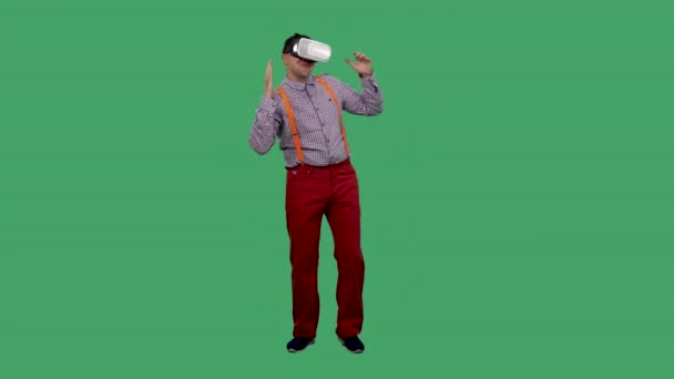 Portrait d'un danseur avec un casque de réalité virtuelle ou des lunettes 3D sur la tête. Un homme avec des lunettes, une chemise avec des bretelles orange en studio sur un écran vert. Mouvement lent. — Video