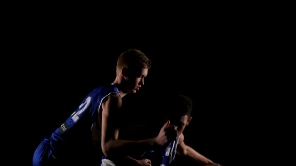 Los atletas se dedican al baloncesto en un estudio oscuro sobre un fondo negro. Lucha por una pelota de baloncesto entre dos jóvenes, rivales. En cámara lenta. De cerca.. — Vídeo de stock