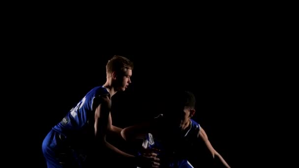 Dois jovens desportistas estão praticando basquete em um estúdio escuro em um fundo preto. Um jogador tenta roubar uma bola de basquete de um adversário. Movimento lento. Fechar. — Vídeo de Stock