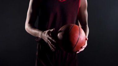 Siyah arka planda karanlık bir stüdyoda genç bir basketbolcu. Bir sporcunun eline yakın durun, bir basketbol topunu tutun, kaydırın, bir elden diğerine fırlatın. Yavaş çekim.