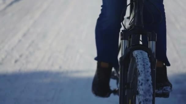 Man rijden fiets op een besneeuwde dag, gladde wegomstandigheden. Close-up van mannenvoeten die trappen. Fietswielen in de sneeuw. Koerier levering van voedsel op de fiets langs een besneeuwde straat. Langzame beweging. — Stockvideo