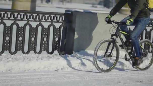 Expresslieferung von Lebensmitteln mit dem Fahrrad während der Sperrung und Coronavirus-Epidemie. Mann mit Schutzmaske und gelbem Thermo-Rucksack fährt Fahrrad auf schneebedeckter Straße in winterlicher Stadt. Zeitlupe. — Stockvideo