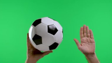 Bir erkek el klasik bir siyah-beyaz futbol topunu tutuyor ve ikinci el de açık bir avuç içi, serbest tekme ile anahtar kromatikliğin stüdyo yeşil ekranında izole edilmiş bir eli gösteriyor. Ağır çekim. Kapat..