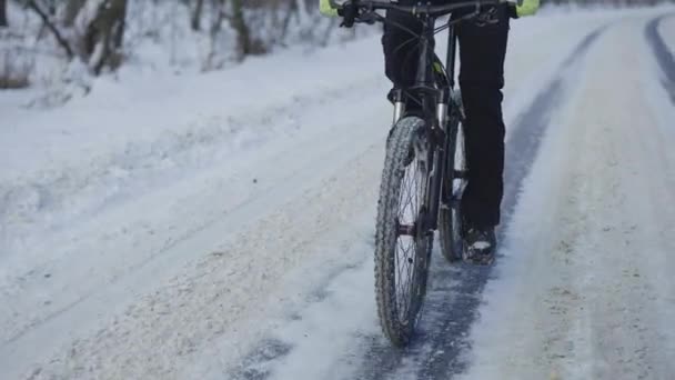 Kerékpározás télen egy havas erdőben. A kerékpáros egy csúszós aszfaltozott úton utazik. A férfi lábak pedáloznak. Egy mozgó bicikli közelsége. Extrém téli biciklizés. Lassú mozgás.. — Stock videók