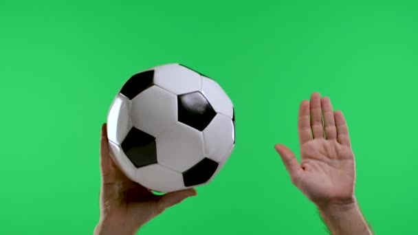 Uma mão masculina segura uma bola clássica de futebol preto e branco e a segunda mão mostra uma mão com uma palma aberta, pontapé livre, isolada em uma tela verde estúdio de cromaticidade chave. Movimento lento. Fechar. — Vídeo de Stock