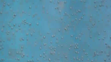 Birçok oksijen kabarcığı berrak maden suyunda mavi arka plana doğru yükselir. Ağır çekim. Kapat..