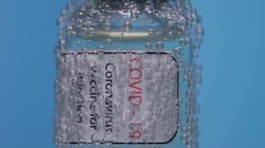 Coronavirus aşı şişesi. Mavi arka planda su kabarcıklarıyla kaplı. Coronavirus 19 tedavi görmüş. Coronavirus tedavisi konsepti, salgın sırasında klinik deneyler. Ağır çekim. Kapat..