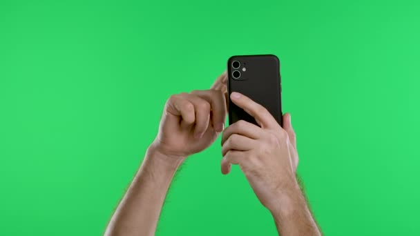 Las manos masculinas sostienen un teléfono inteligente verticalmente contra el fondo de una tecla croma de pantalla verde. Las manos tocan la pantalla táctil, desplázala. Gadgets y el concepto de la gente moderna. En cámara lenta. De cerca.. — Vídeos de Stock