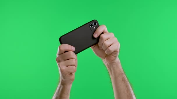 Чоловічі руки тримають смартфон горизонтально на тлі зеленого екрану ключа хрому. Гра в онлайн ігри, соціальні мережі, перегляд відео. Повільний рух. крупним планом . — стокове відео