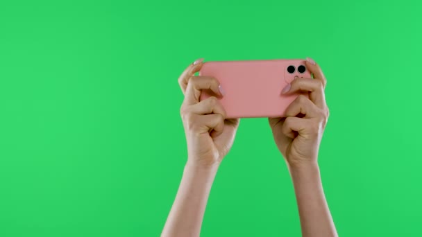 Las manos femeninas sostienen el teléfono inteligente horizontalmente contra el fondo de la pantalla verde de la tecla de croma. Jugamos juegos en línea, en las redes sociales, ver videos. En cámara lenta. De cerca.. — Vídeos de Stock